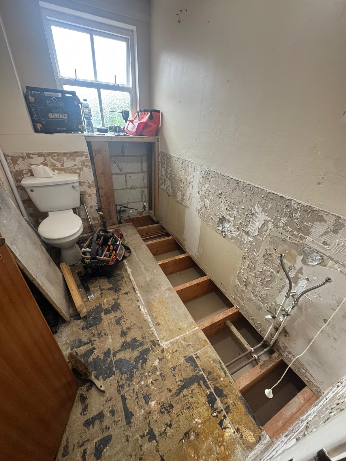 Old bath removed and floor lifted to reroute pipework during a walk-in shower conversion by Adsett Bathrooms
