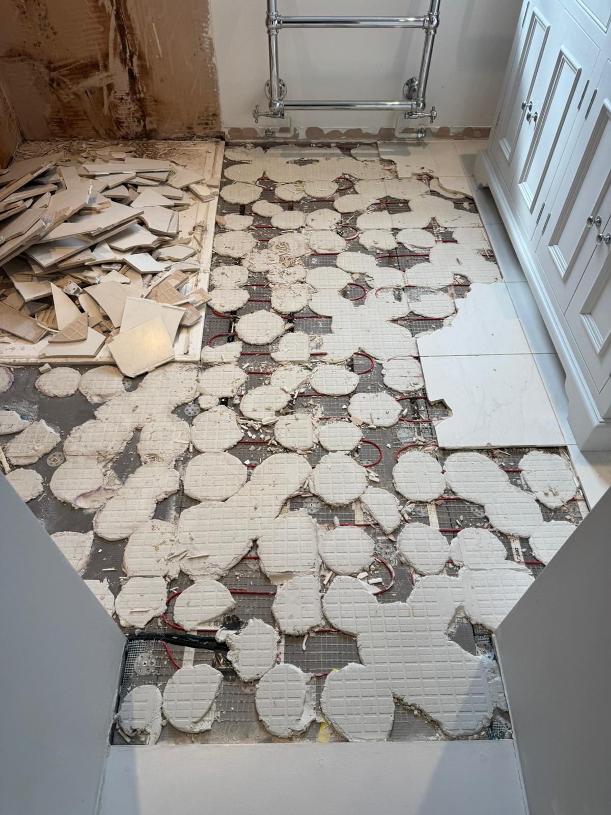 Loose floor tiles lifted to expose underfloor heating, ready for re-tiling by Adsett Bathrooms