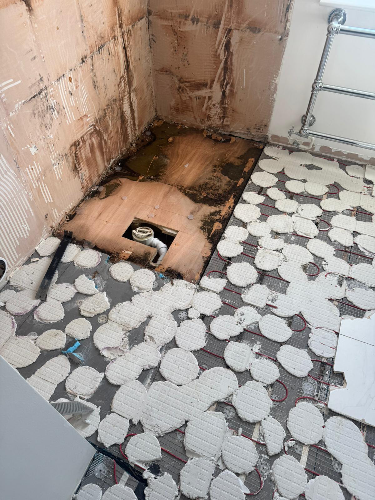 Damp, water-stained subfloor exposed where the leak had been tracking, before repair by Adsett Bathrooms