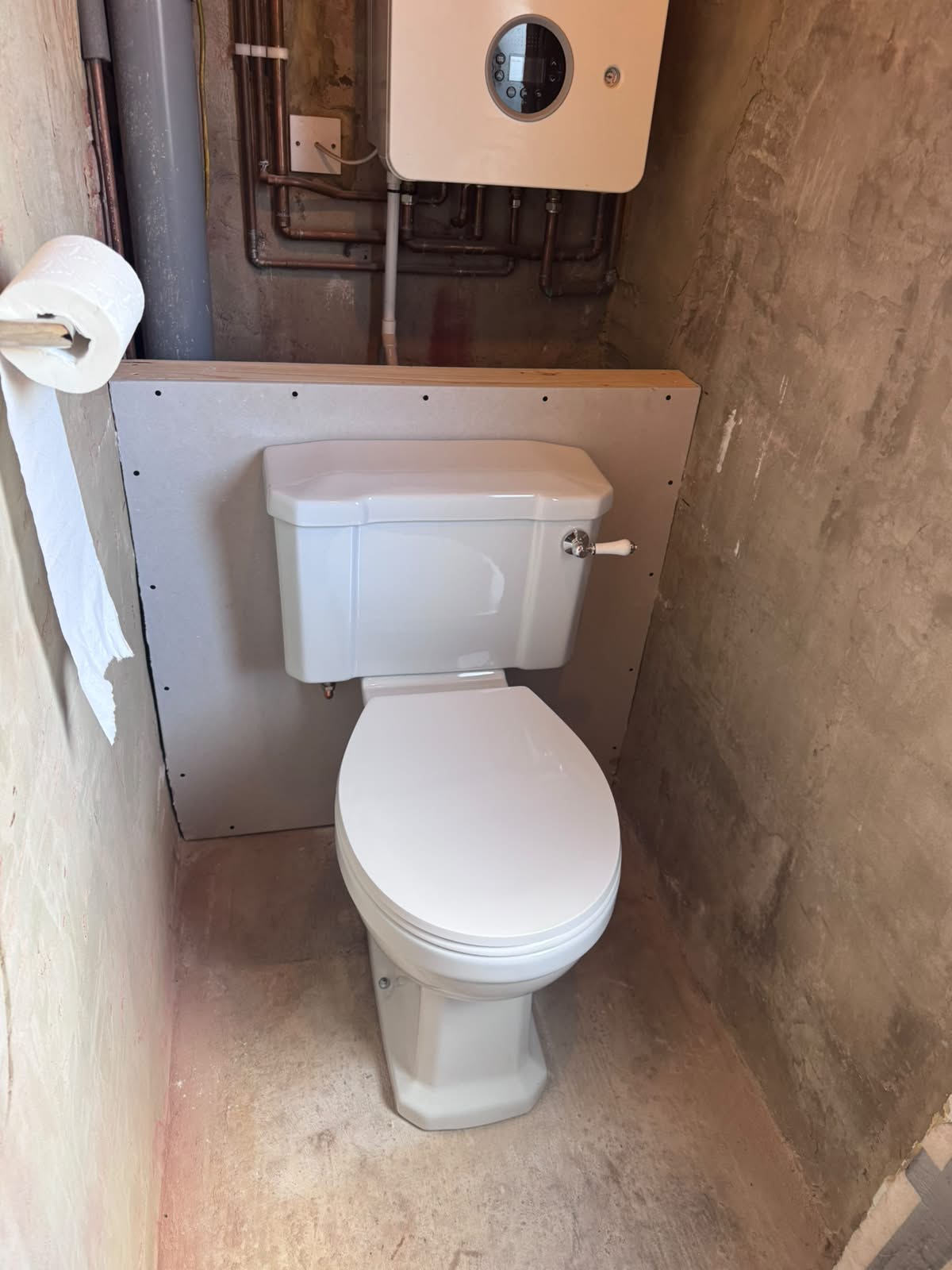 Traditional-style comfort height toilet fitted against a new boarded stud wall by Adsett Bathrooms in West Sussex