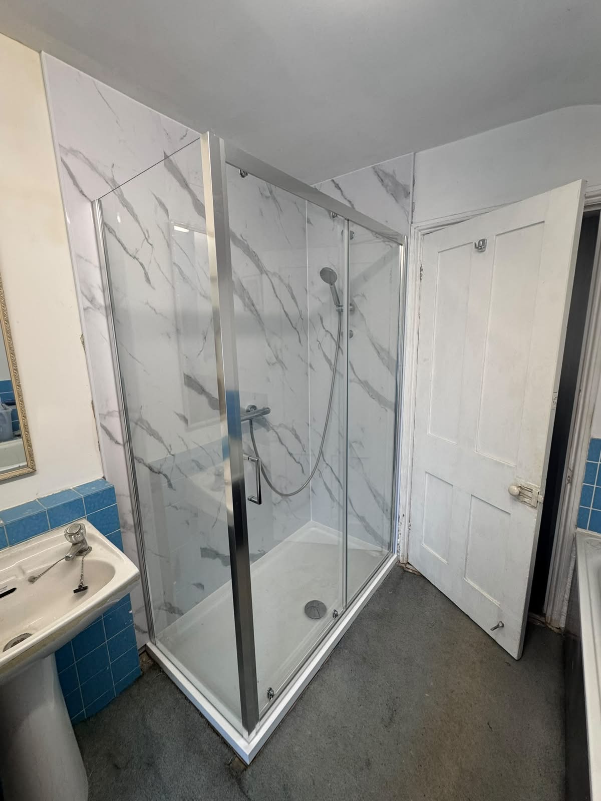 New low profile shower tray at floor level with a sliding-door enclosure and marble-effect wall panels, fitted by Adsett Bathrooms in West Sussex