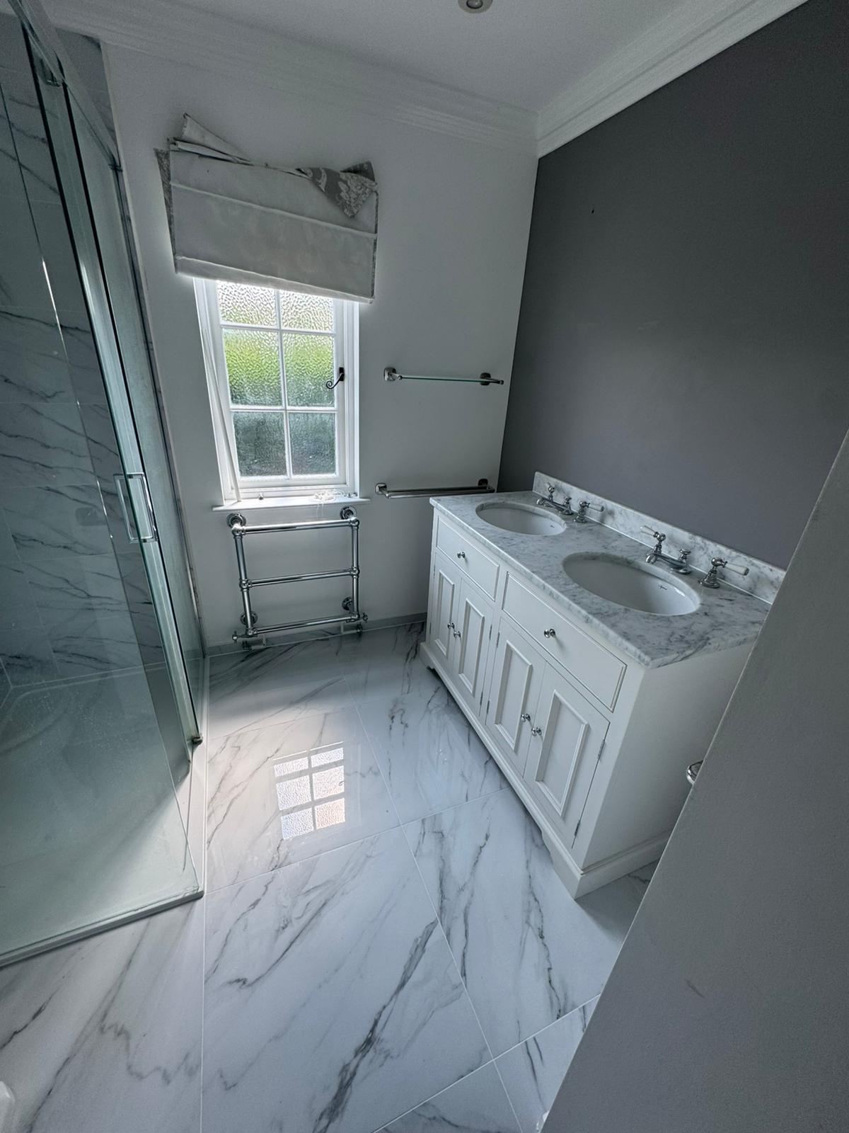 Finished marble bathroom with double vanity, twin basins and traditional towel rail by Adsett Bathrooms in West Sussex