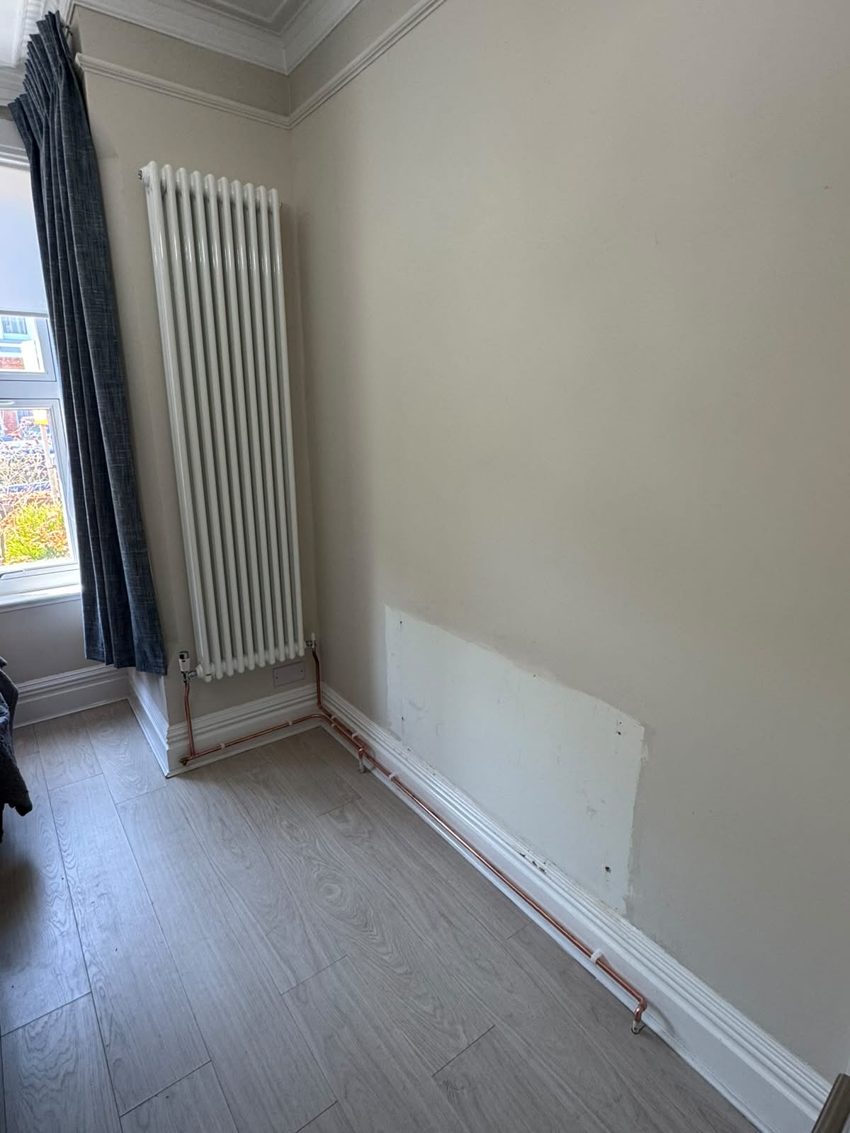 Tall white vertical column radiator moved to another wall beside a window, with surface-mounted copper pipework, by Adsett Bathrooms in West Sussex