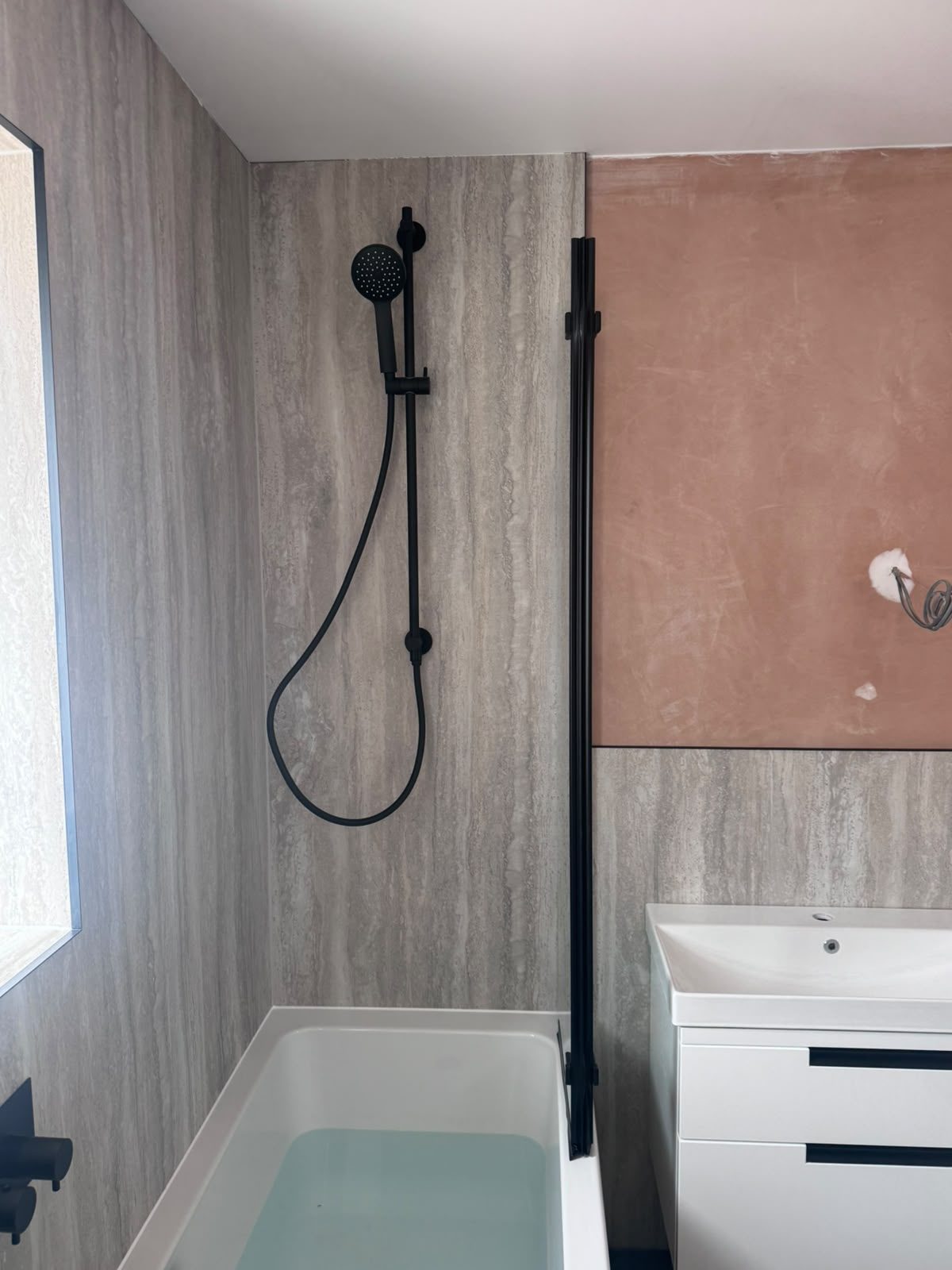Matt black shower and bath with stone-effect wall panelling in a West Sussex bathroom renovation