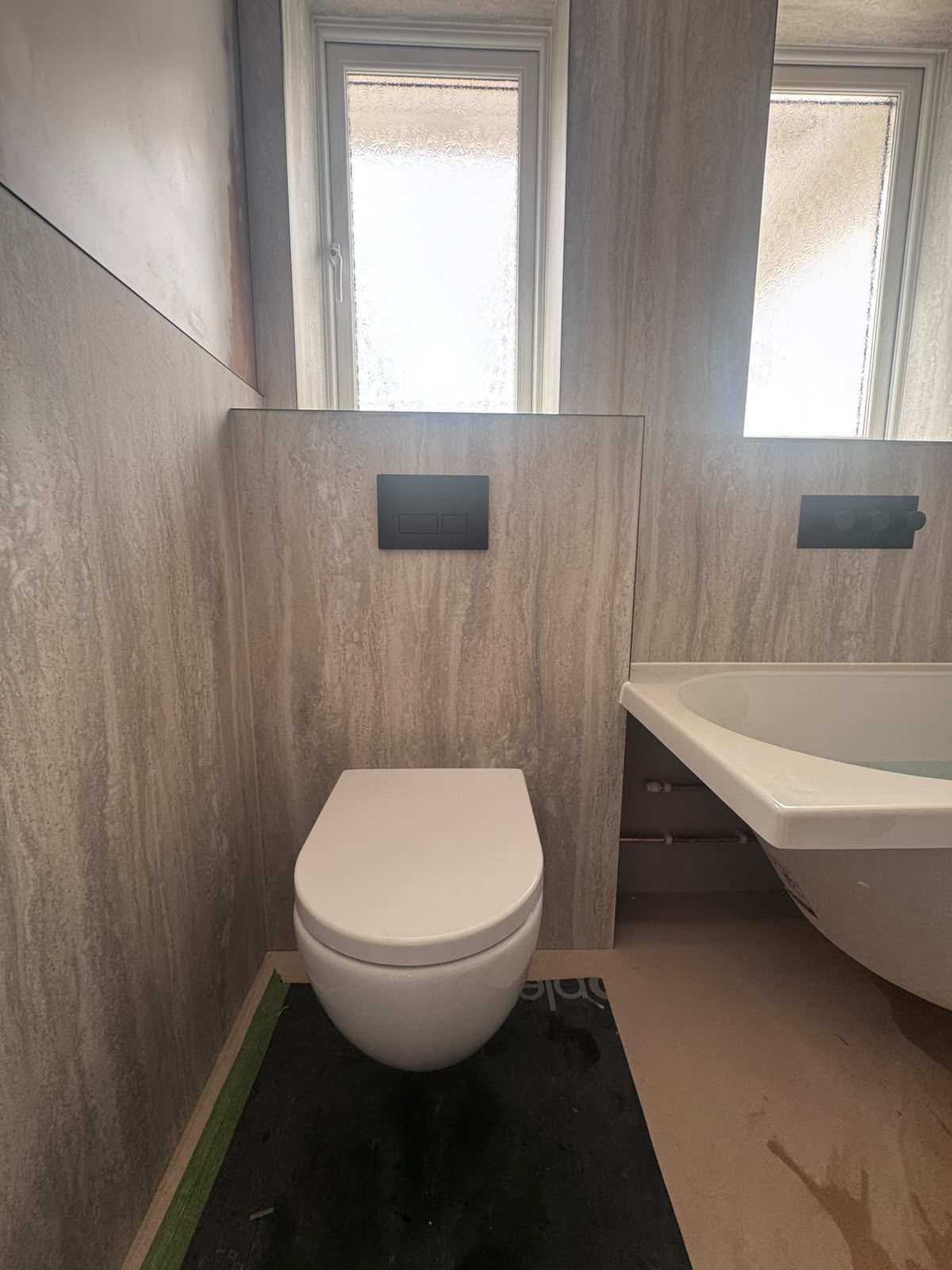 Wall-hung toilet with matt black flush plate fitted by Adsett Bathrooms